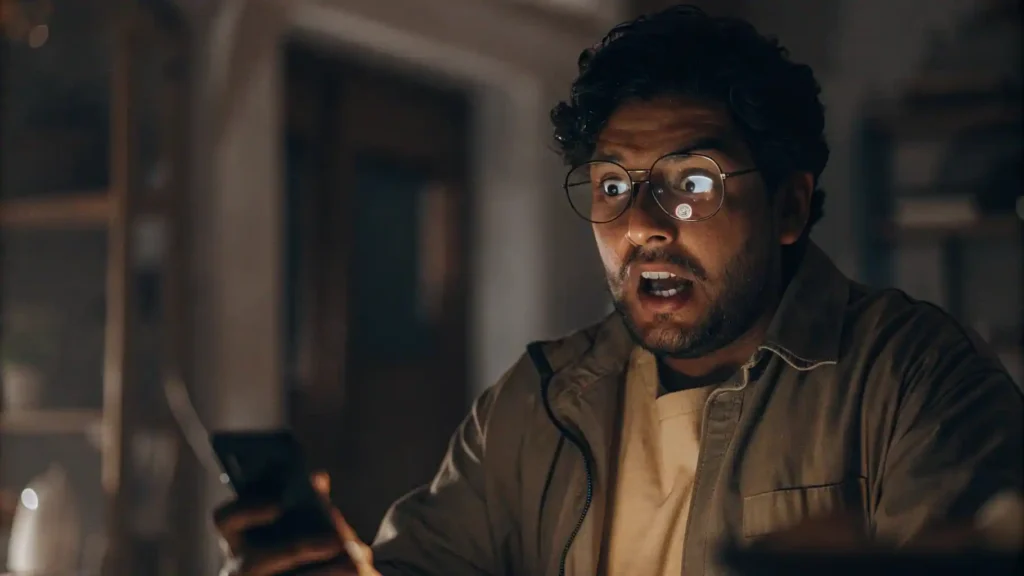 Hombre hispano mirando su celular con cara de shock y preocupación, como si hubieran robado su cuenta de WhatsApp.